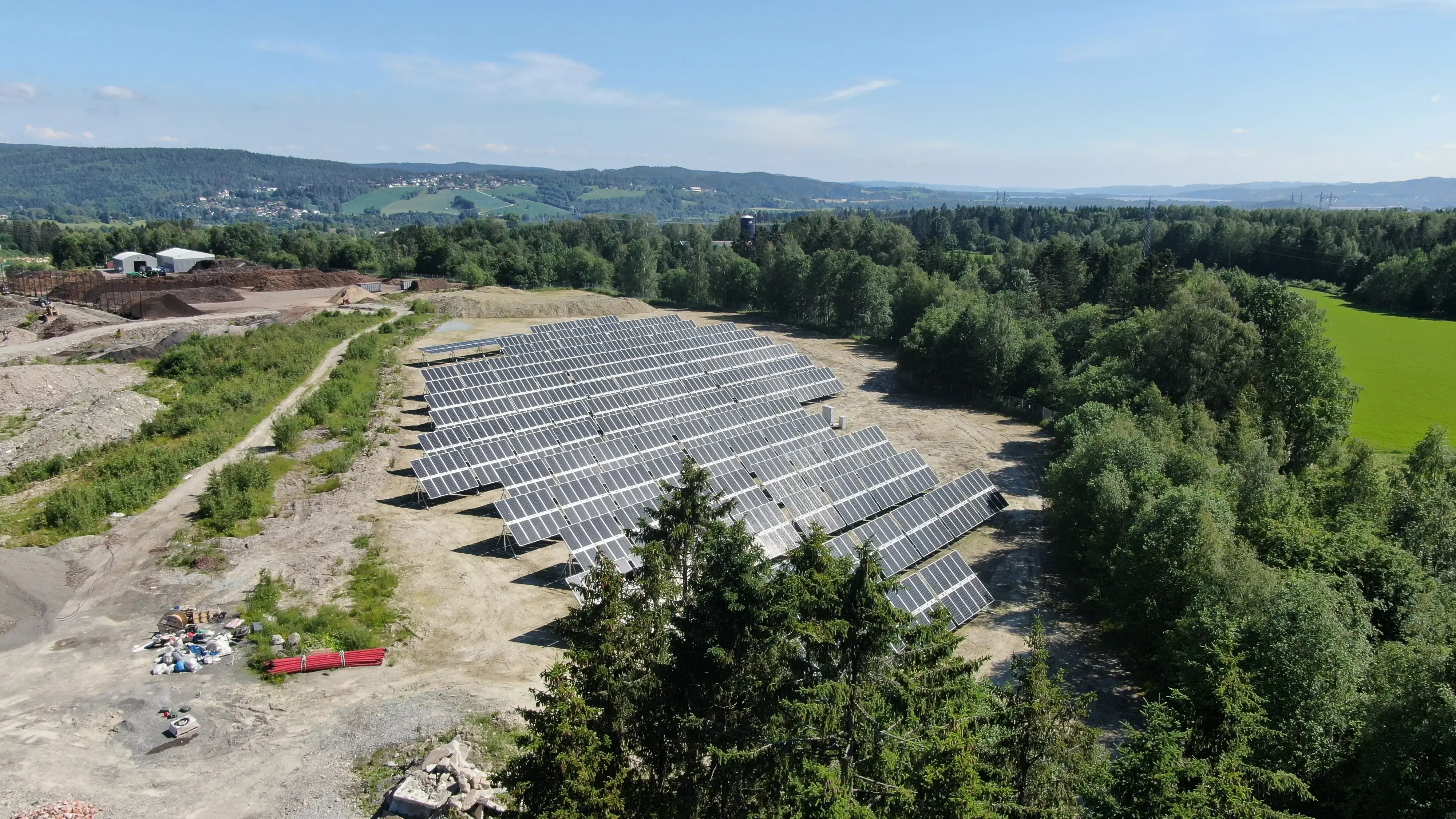 Aerial view of a ground-mounted solar farm on a cleared site surrounded by forest and farmland