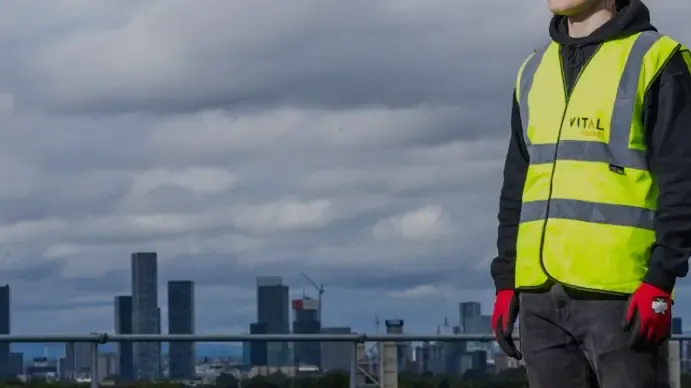 Project worker in a hi-vis vest and work gloves with the city skyline behind