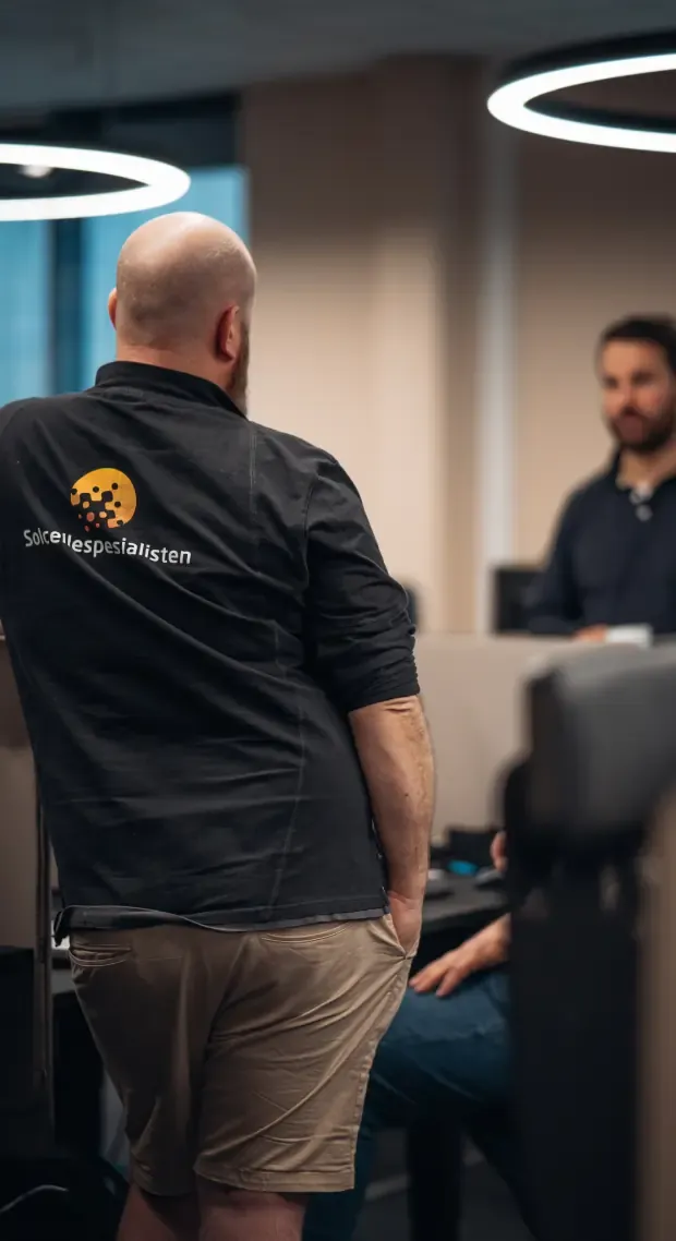 Employee in a Solcellespesialisten jacket talking with a colleague in the office
