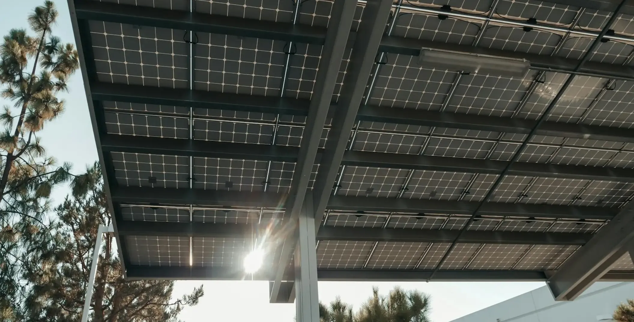 Sunlight shining through solar panels mounted on an open steel frame, seen from below